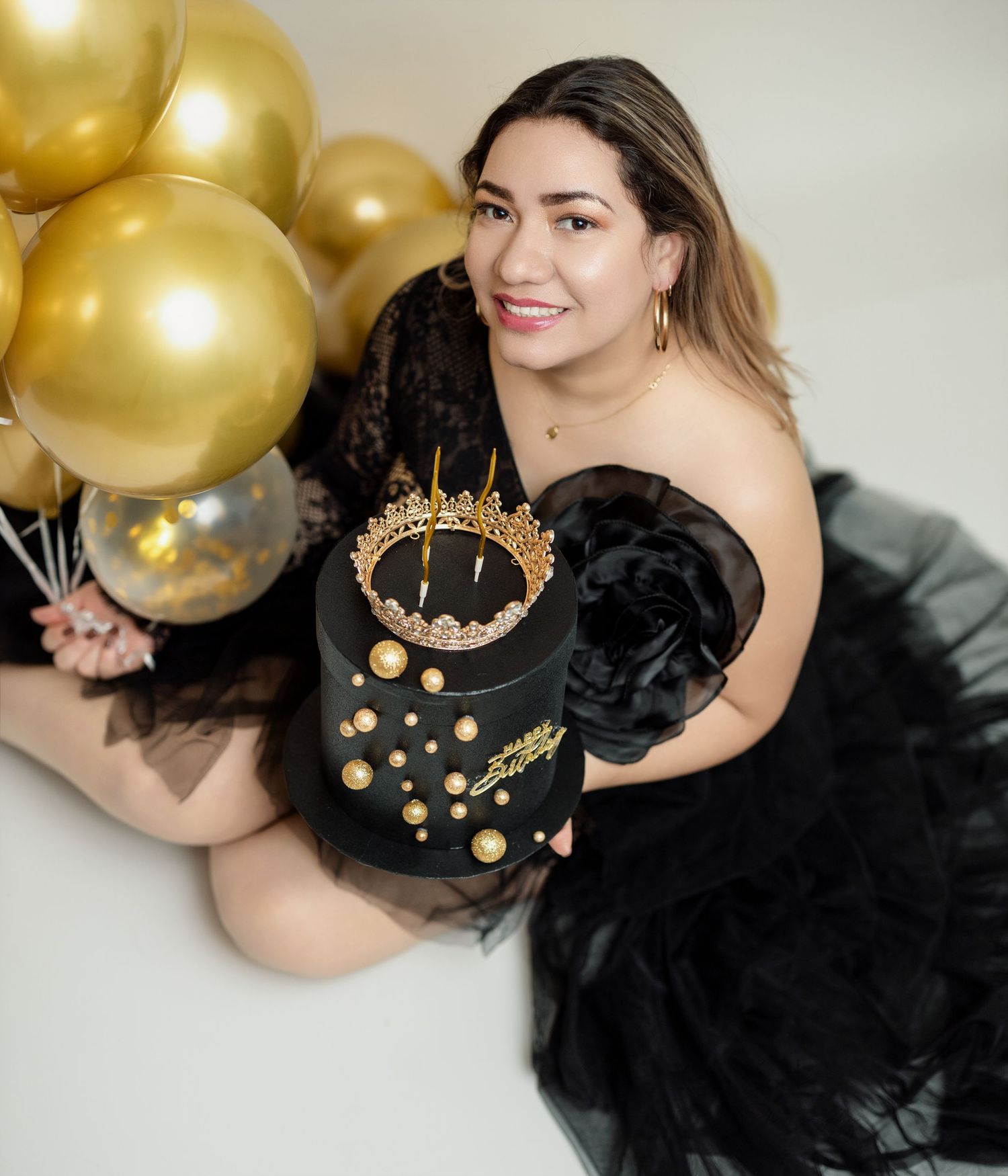A celebratory scene with gold balloons and a black decorated cake with crown details.