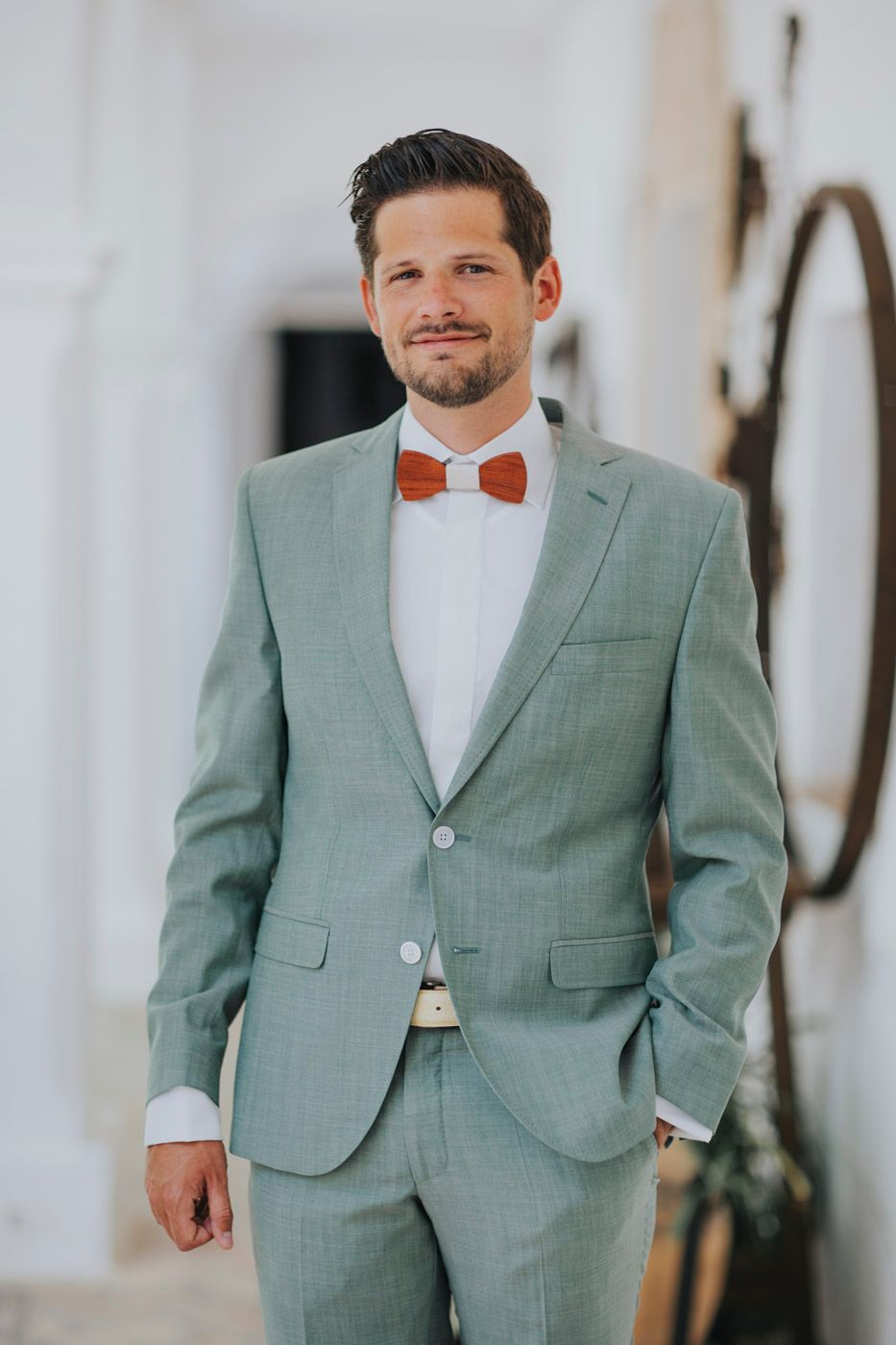 Wedding day attire featuring a mint green suit and orange bow tie against a white background.