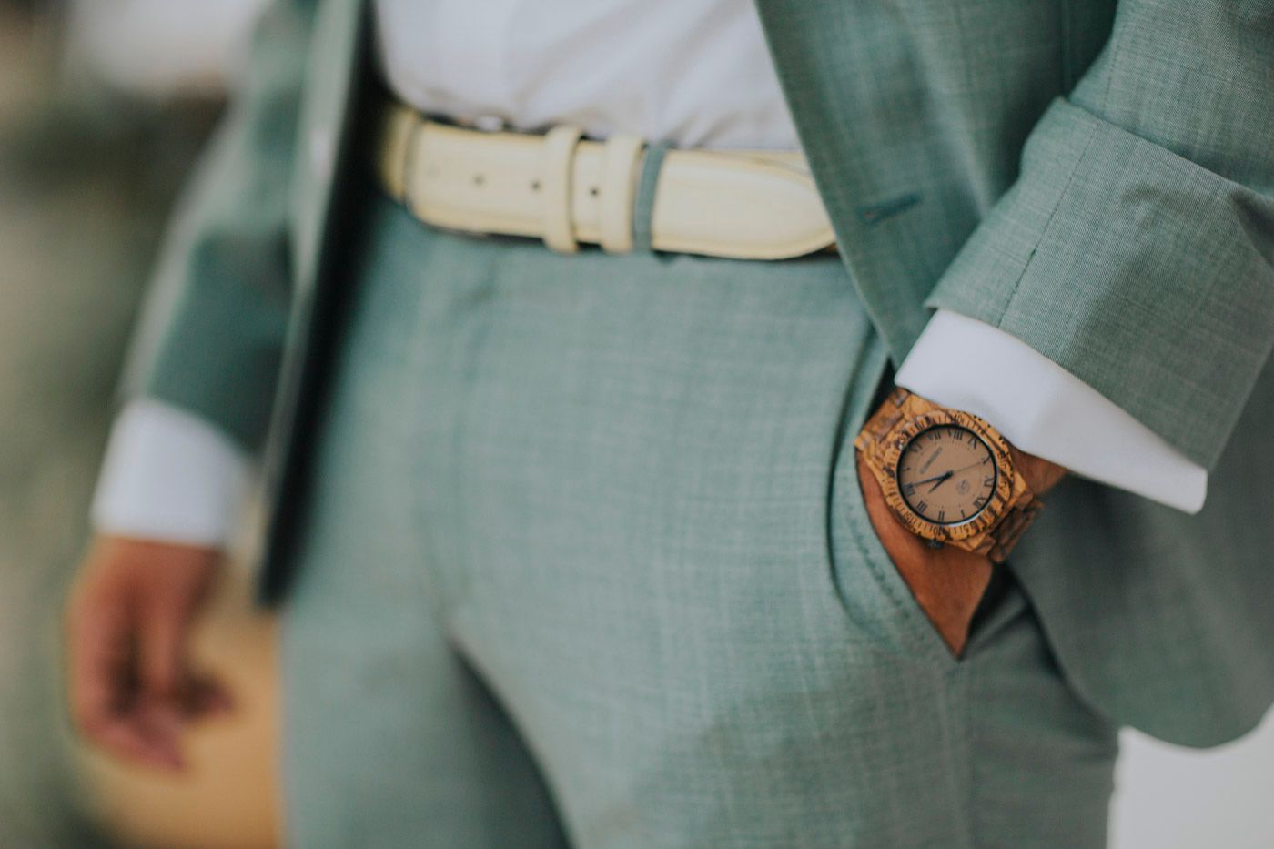 Close-up detail of a light green suit with brown leather watch and cream colored belt.