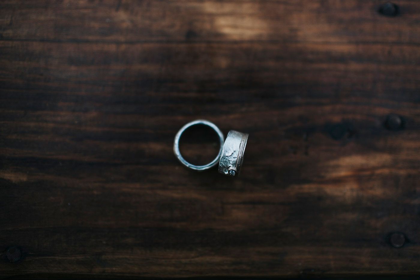 Two elegant wedding rings rest on a dark wooden surface with rustic grain texture.
