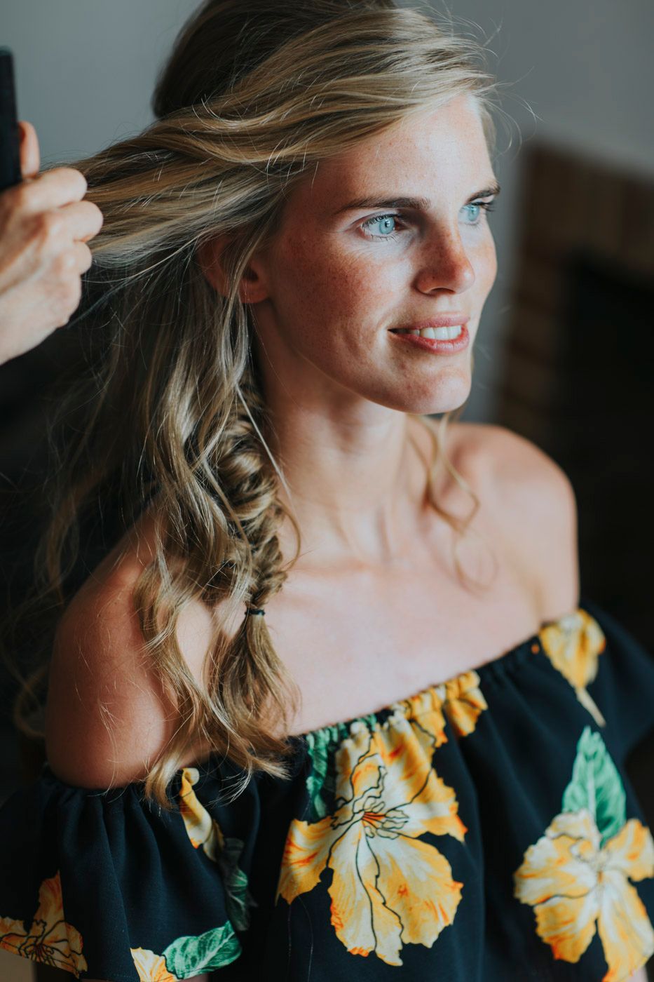 A close up portrait of someone wearing a black floral dress with yellow and green flowers against a soft background.