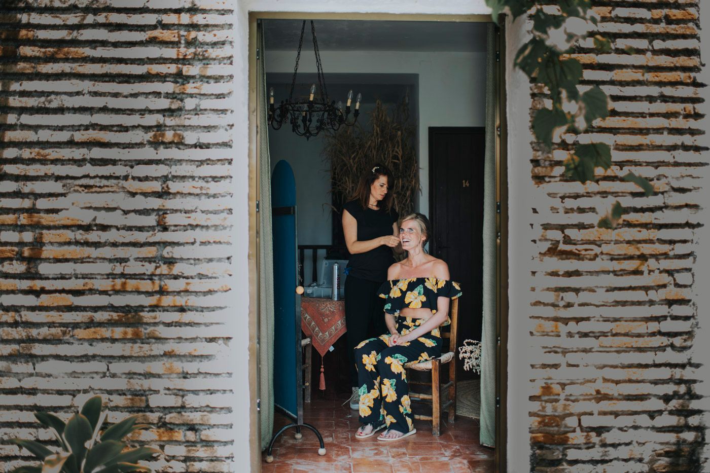 Two people stand in a rustic doorway with weathered brick walls and greenery growing up the sides.