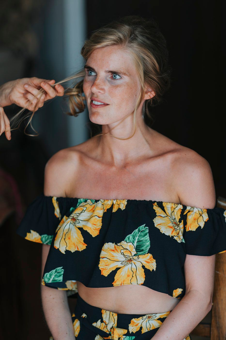 Portrait of someone in an off-shoulder floral crop top with yellow and green flowers against a dark background.