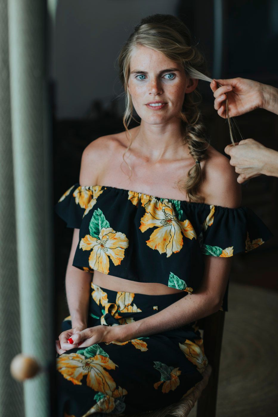 A model in a tropical floral off-shoulder crop top and matching skirt ensemble while getting hair styled.