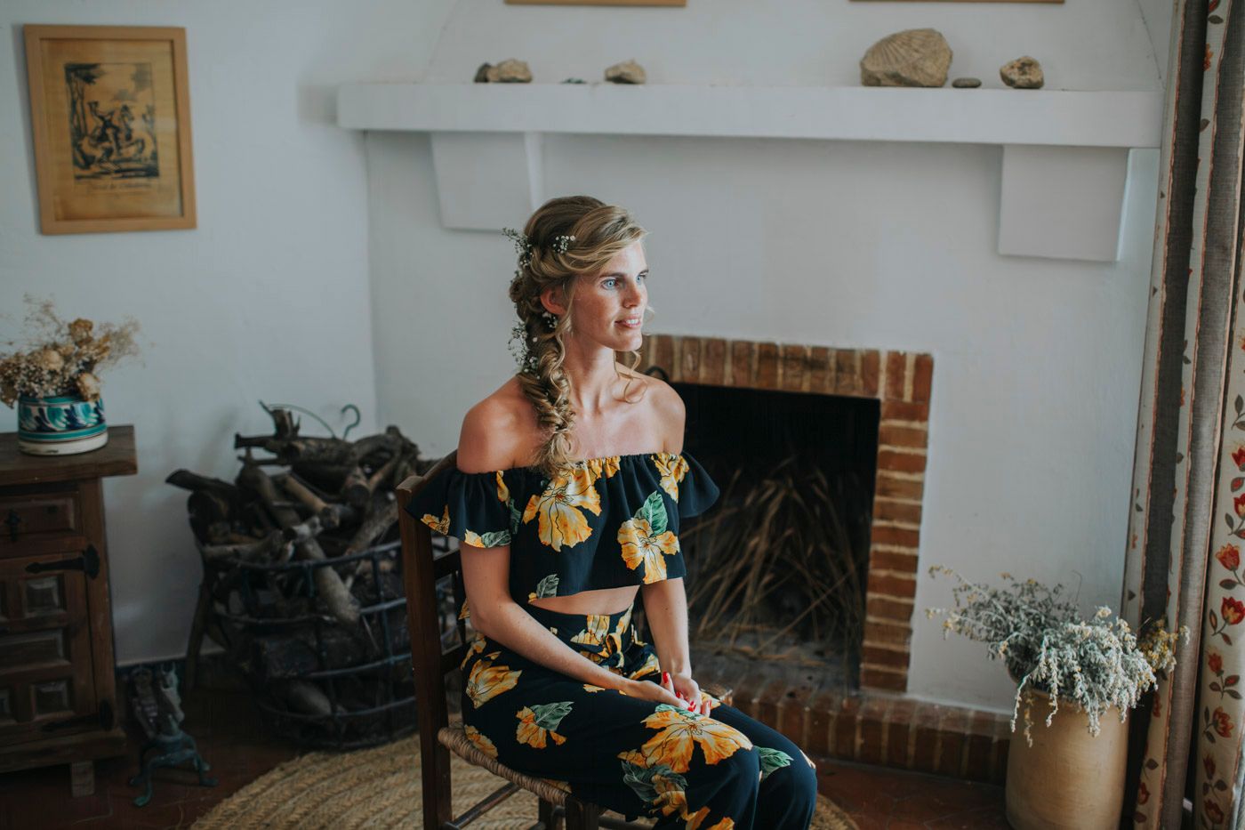 An elegant yellow floral dress photographed against a white fireplace in a cozy interior setting.