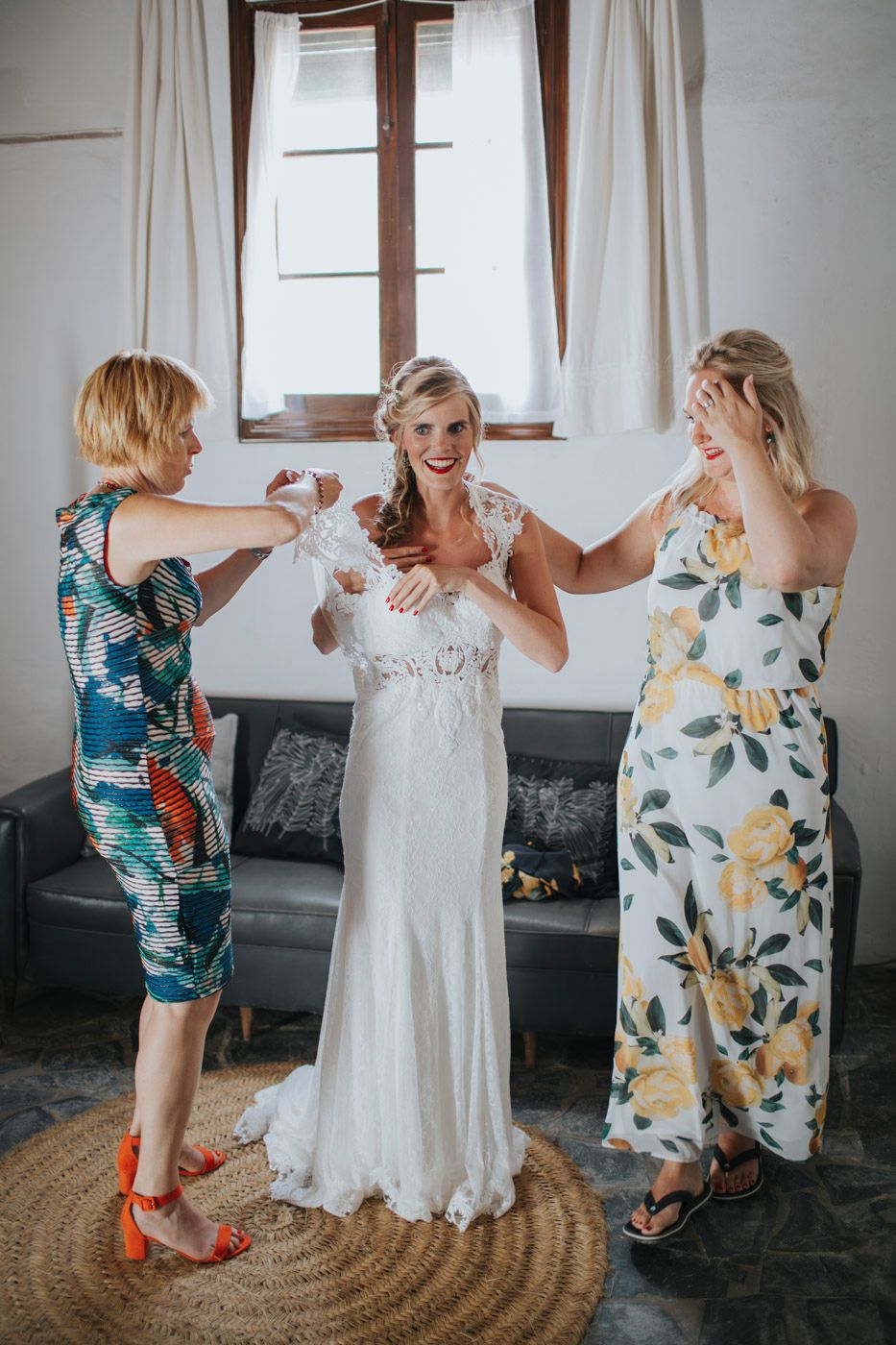 Circle of friends in floral dresses gather joyfully around a bride wearing a lace gown at a wedding celebration.