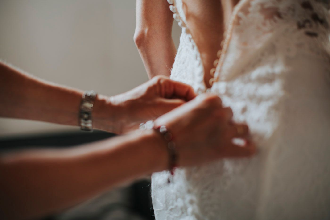 Close-up view of hands delicately adjusting the lacing or buttons on an elegant white lace wedding dress.
