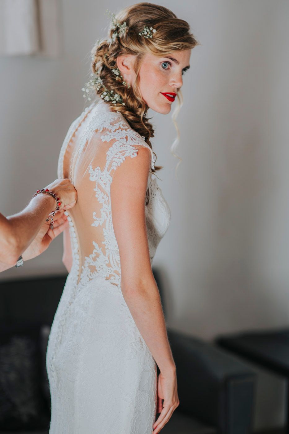 Elegant lace wedding dress with open back detail and braided hairstyle adorned with small white flowers.