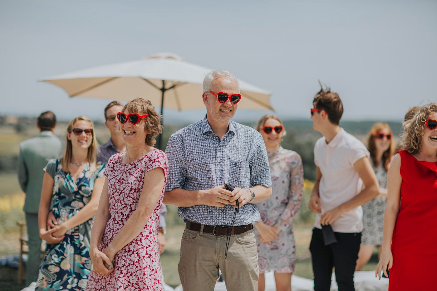 A group of people gather outdoors under white umbrellas on a sunny summer day.