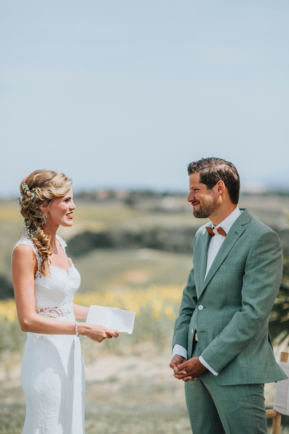 A couple exchanges heartfelt vows during their wedding ceremony against a scenic rural backdrop.