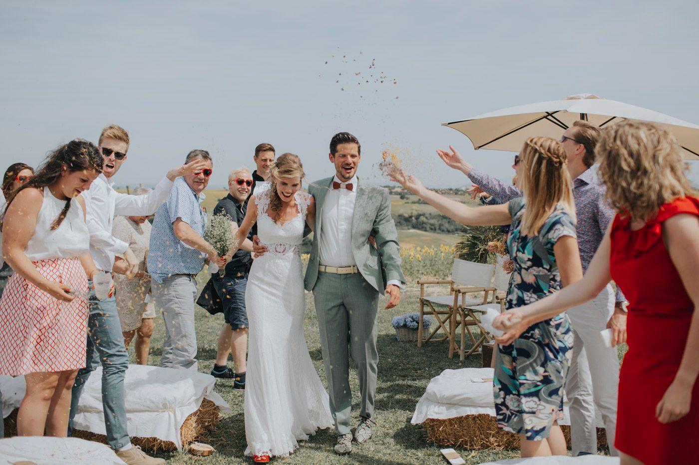 Wedding guests throw petals and celebrate with the newlyweds during an outdoor countryside celebration.