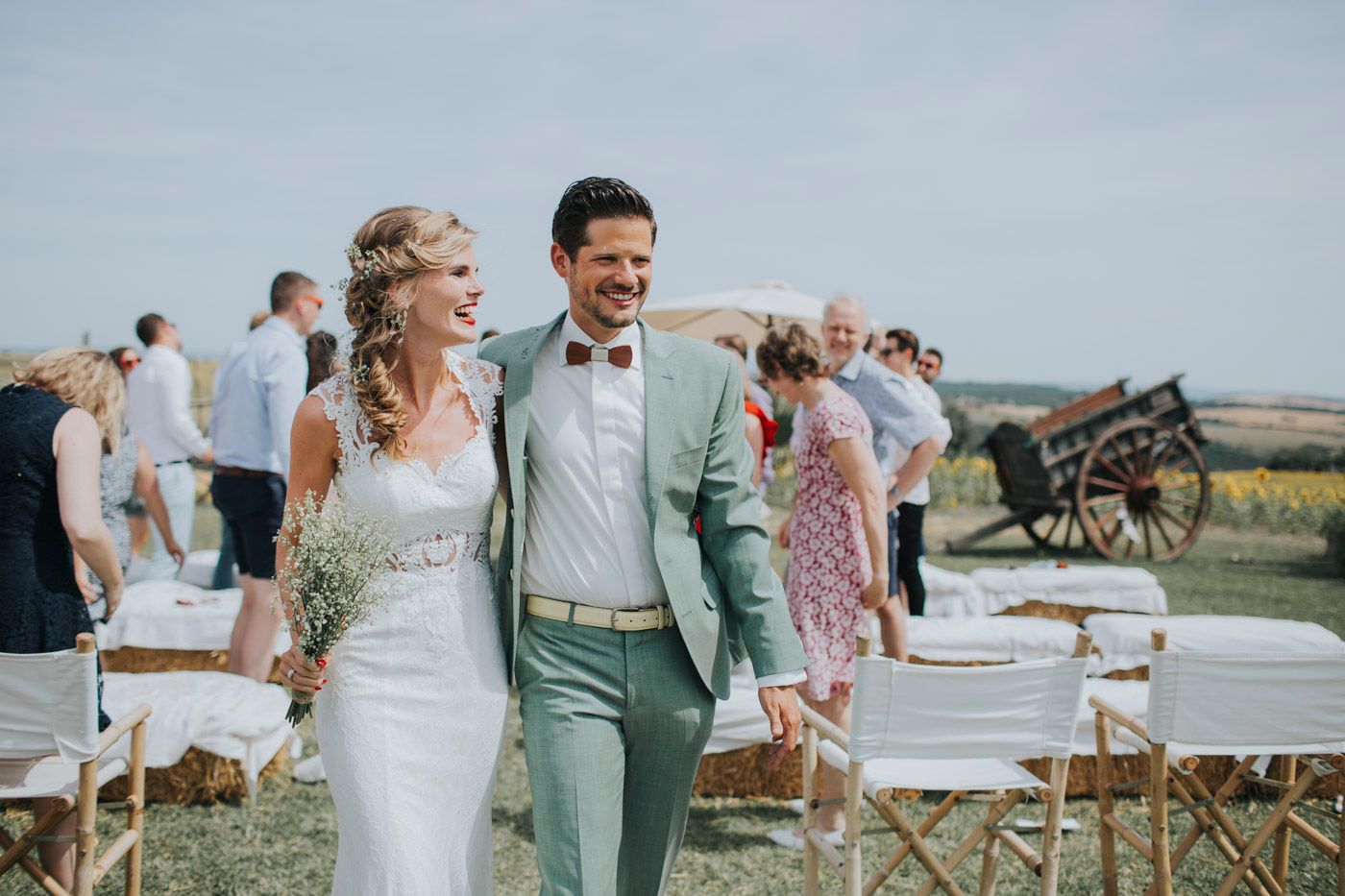 A cheerful wedding couple in mint green and white attire walking together at an outdoor countryside venue.