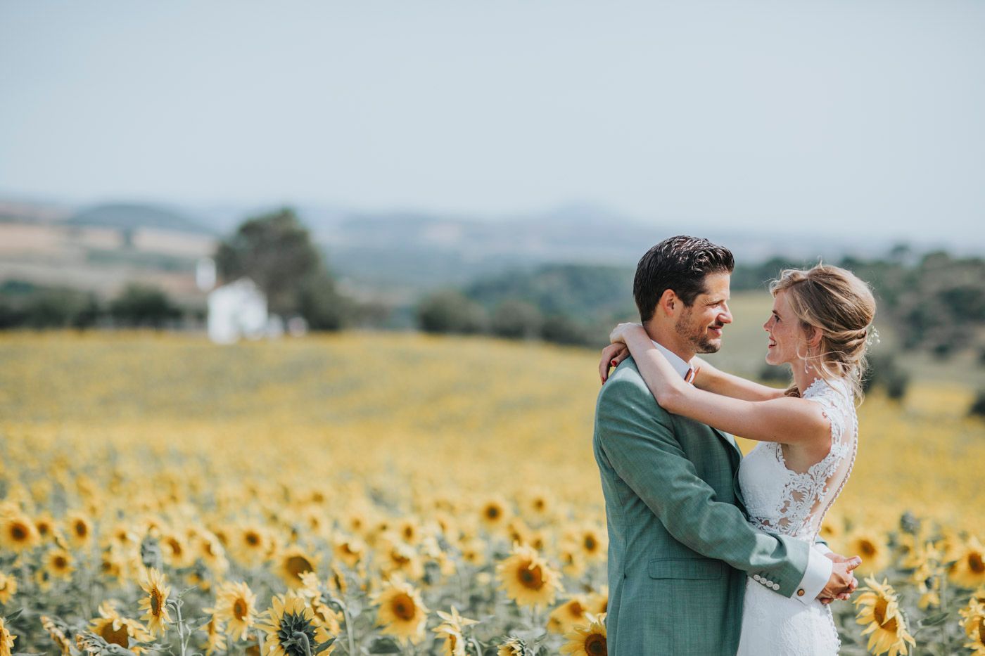 Couple embracing in a romantic moment surrounded by a beautiful sunflower field with rolling hills in the background.