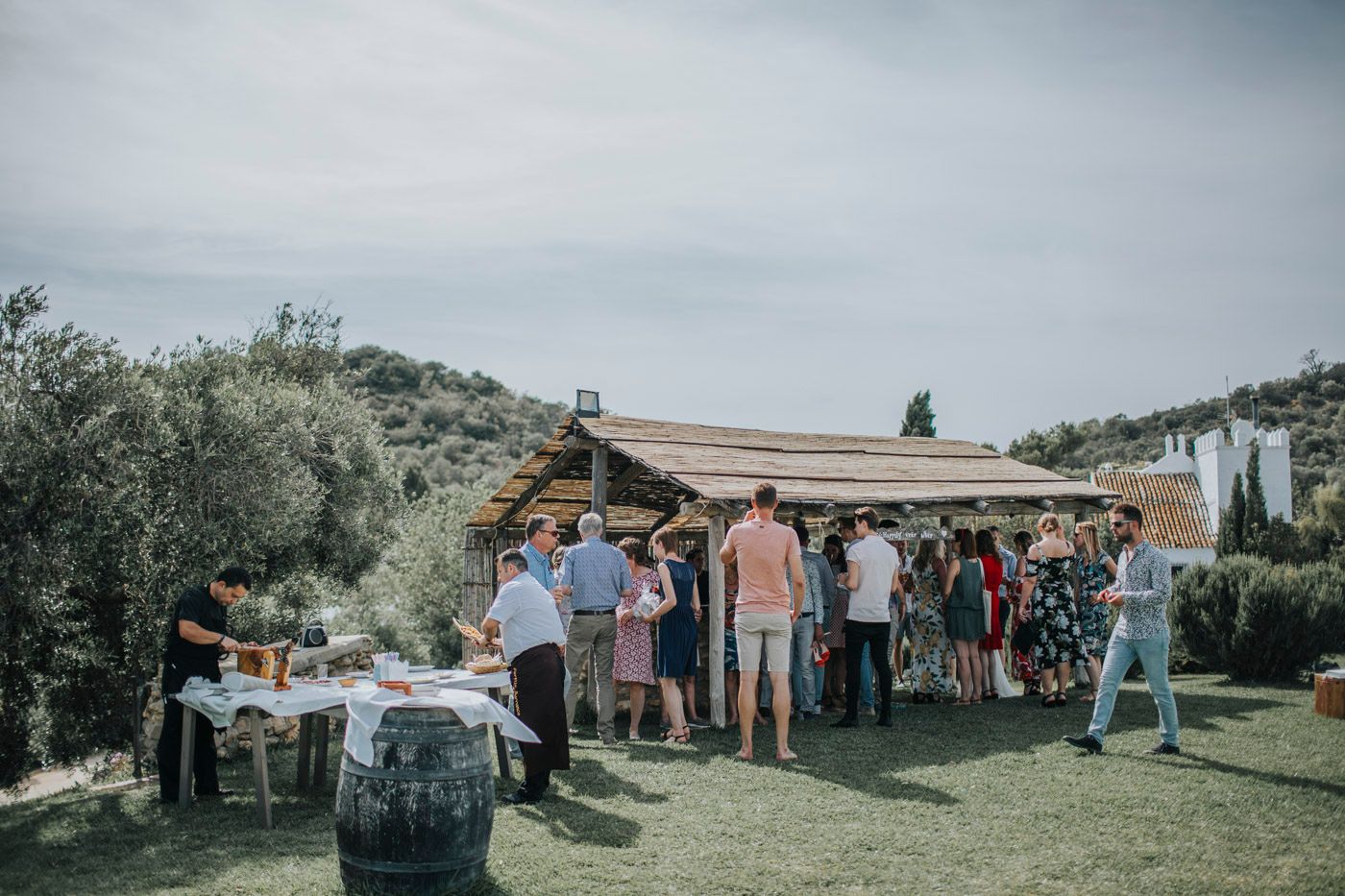 Outdoor gathering with guests mingling around a rustic wooden structure during daytime in a garden setting.