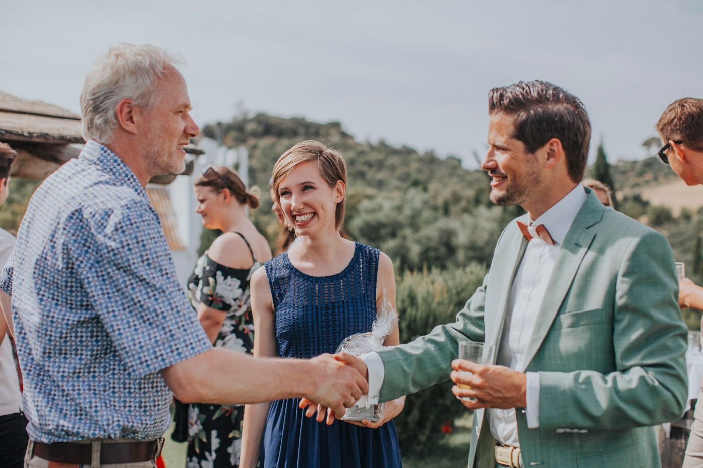 A cheerful outdoor gathering shows people in summer attire sharing handshakes and smiles at a casual event.