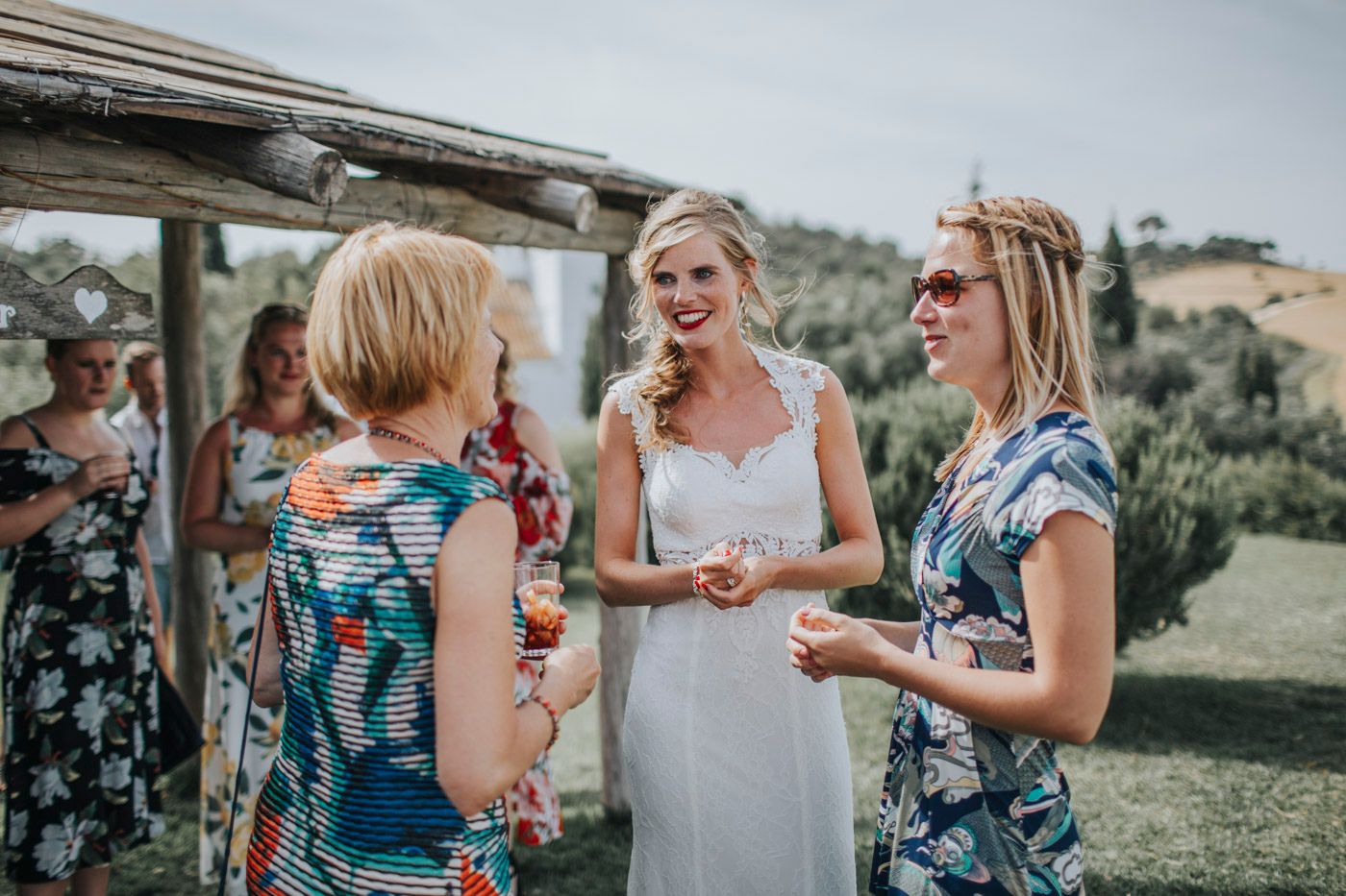 Guests in floral dresses enjoying conversation at an outdoor garden reception during a sunny afternoon.
