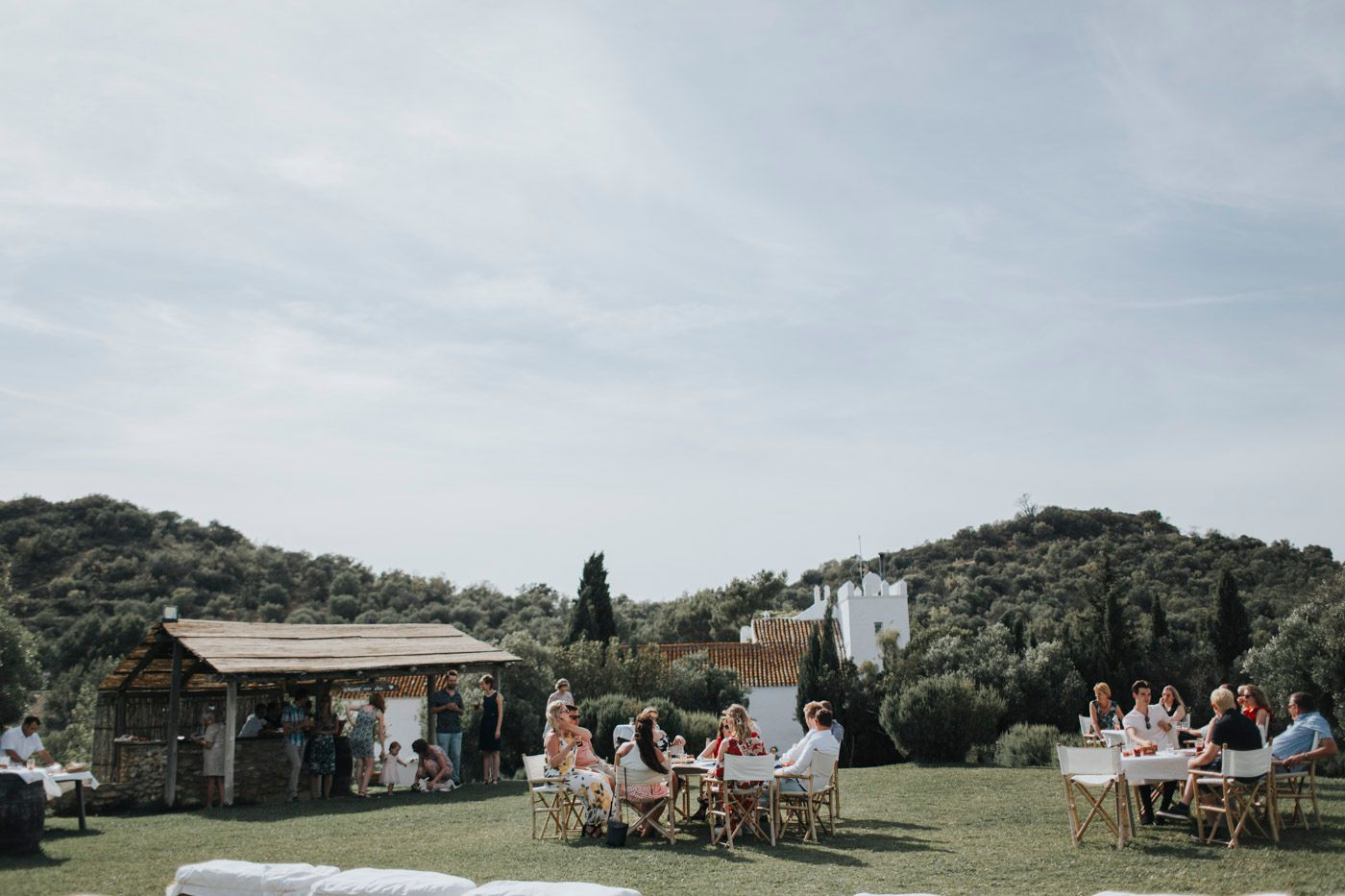 Outdoor wedding ceremony setup with rustic wood gazebo and white chairs on a grassy hillside under cloudy skies.