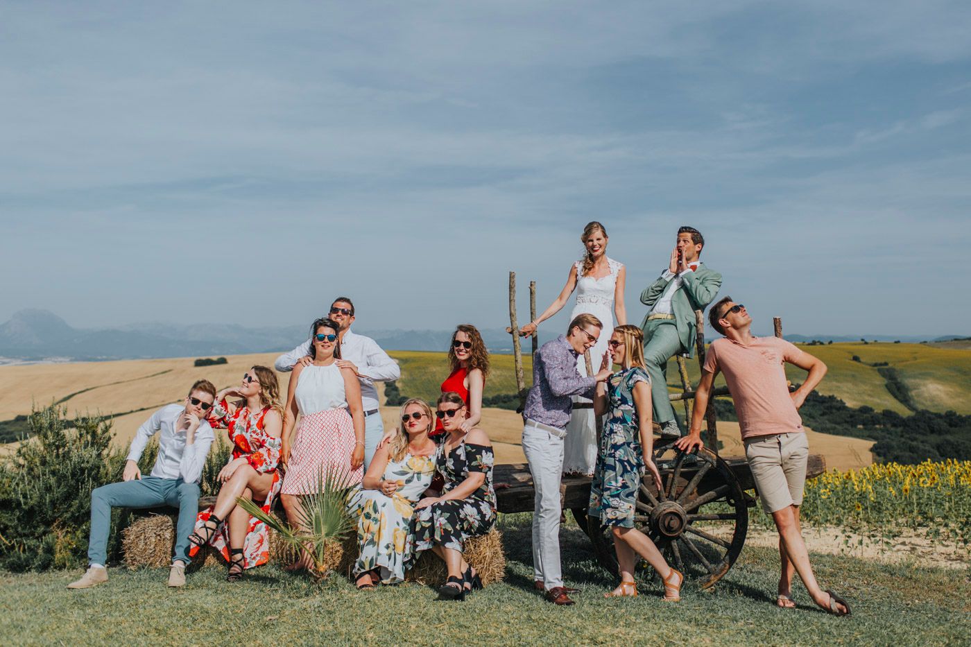 Group photo of joyful guests at an outdoor celebration with scenic hills and countryside in the background.