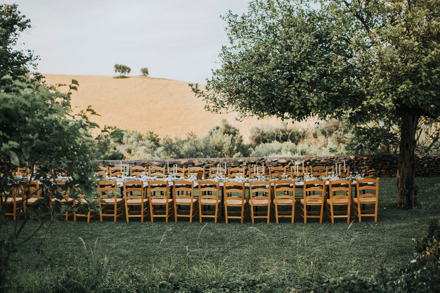 Rows of wooden folding chairs arranged outdoors for a wedding ceremony with rolling hills and trees in the background.