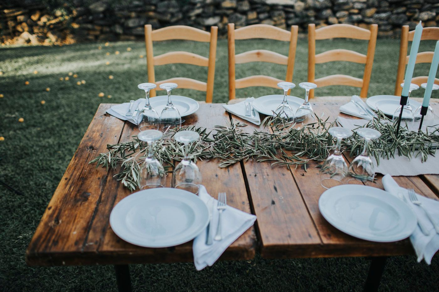 Rustic outdoor dining table set with white plates and delicate greenery centerpiece for an intimate garden gathering.