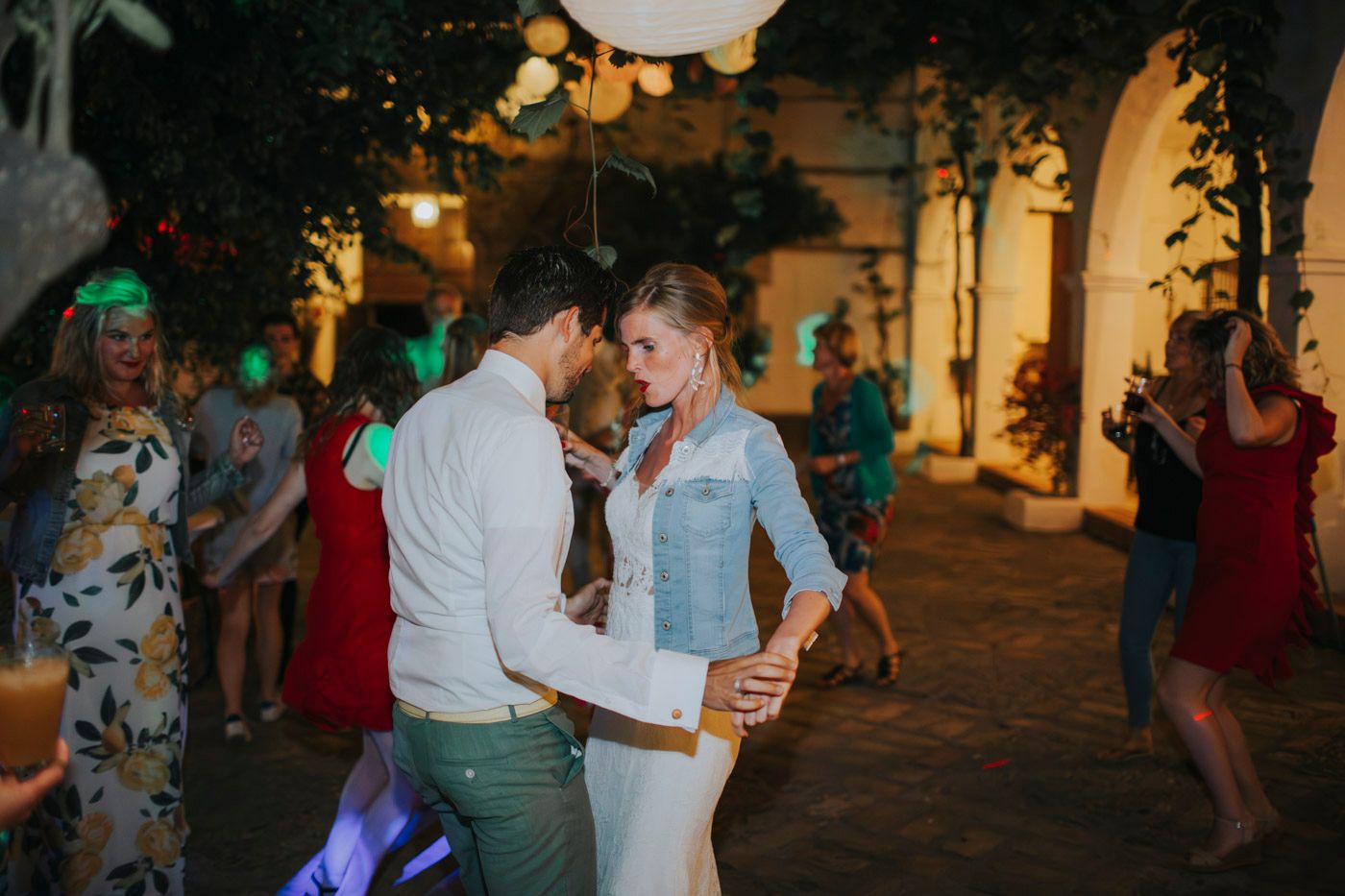 Couples dancing together at a romantic outdoor evening event with string lights and archways in the background.