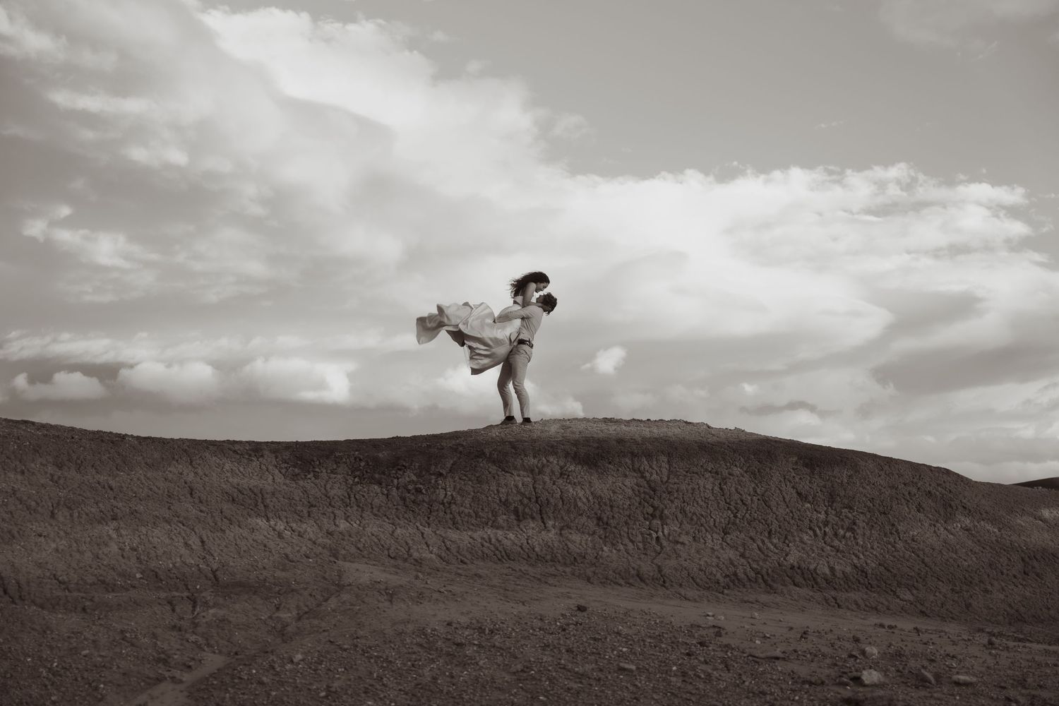 Silhouetted figures stand atop rolling hills against dramatic cloudy sky.