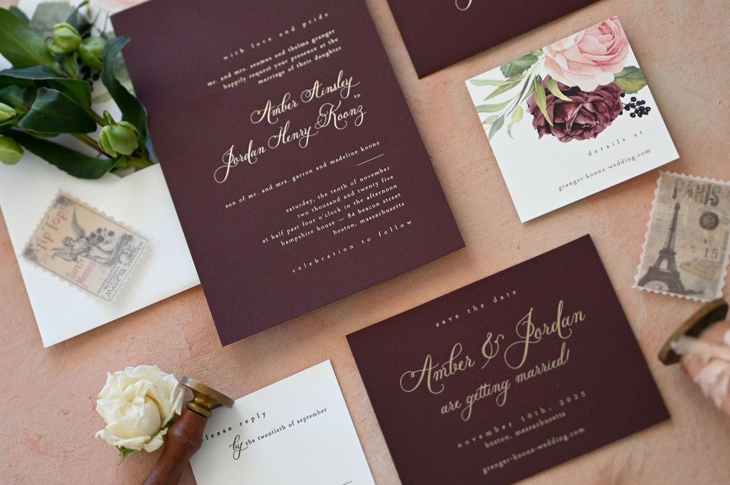 Elegant burgundy wedding invitations with gold calligraphy displayed alongside floral elements and vintage stamps.