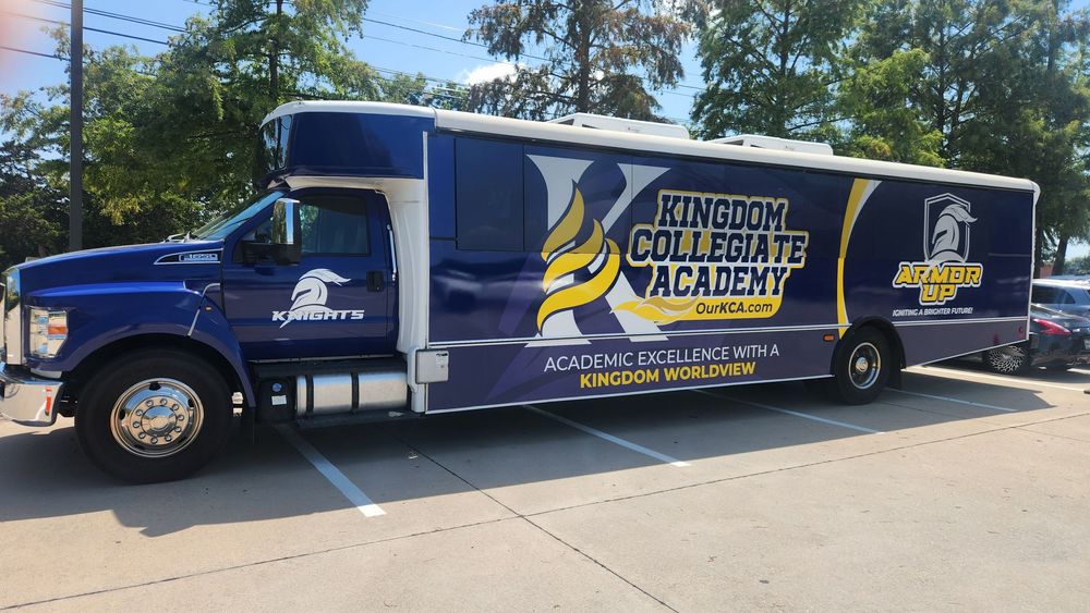 A fleet of dark blue commercial vans with company branding and graphics parked in a row on a sunny day.