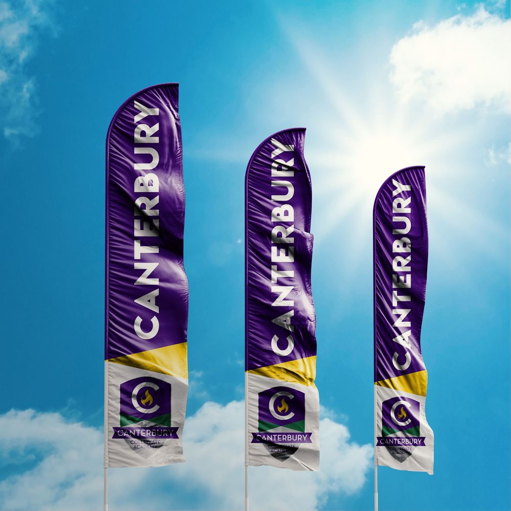 Purple and yellow promotional flags wave against a bright blue sky with white clouds.