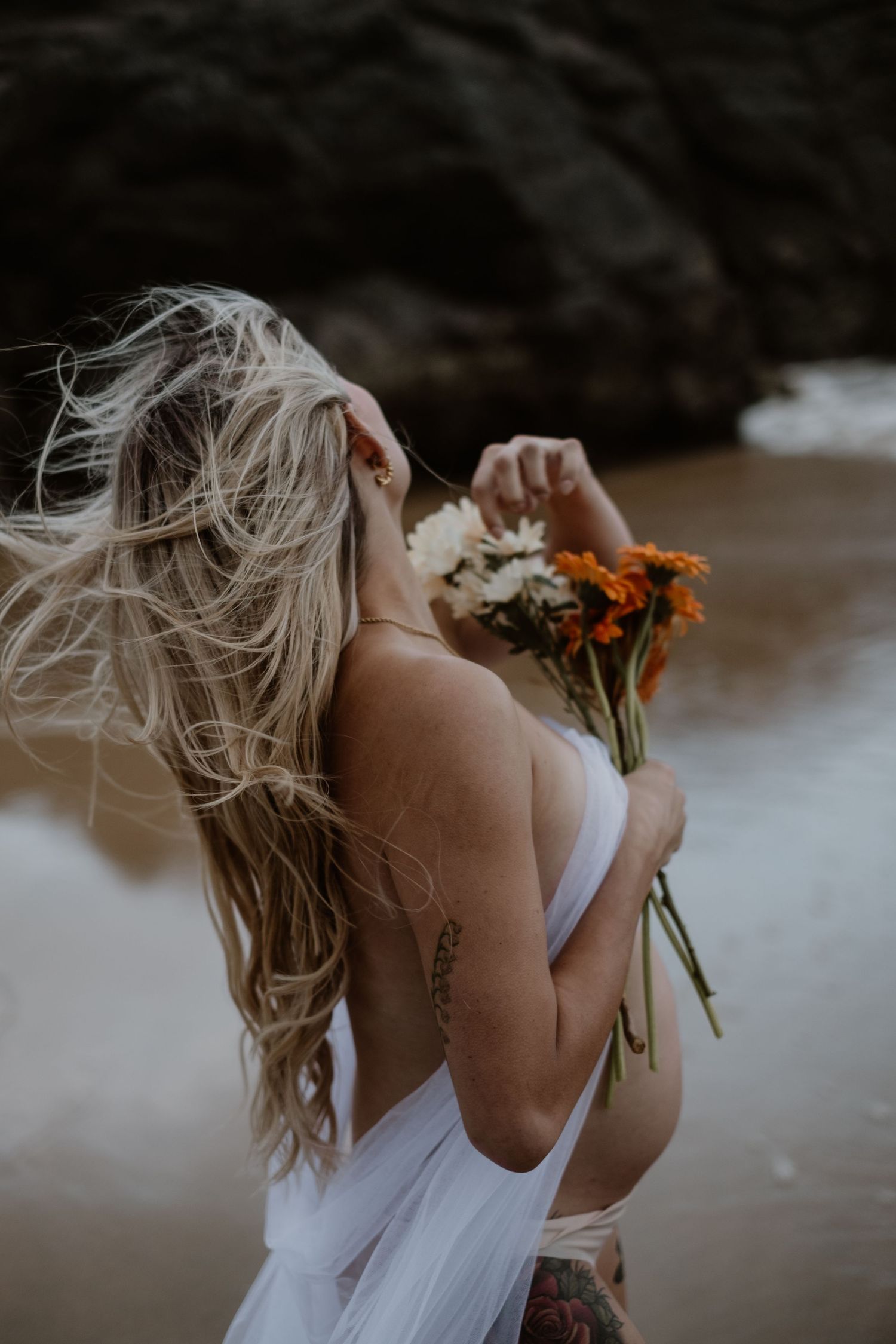 A dreamy portrait with orange flowers and blonde hair blowing in the breeze against a moody background.