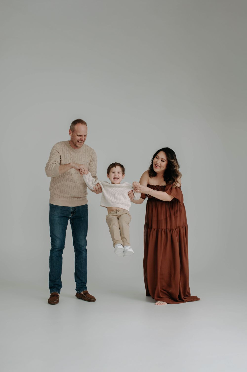 Family lifts child playfully in studio photoshoot against light background.
