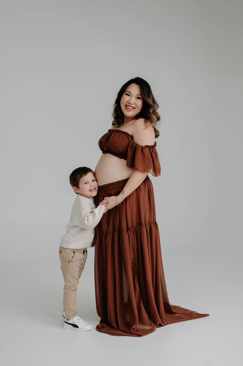 Heartwarming maternity photo with young child hugging pregnant woman in brown dress.