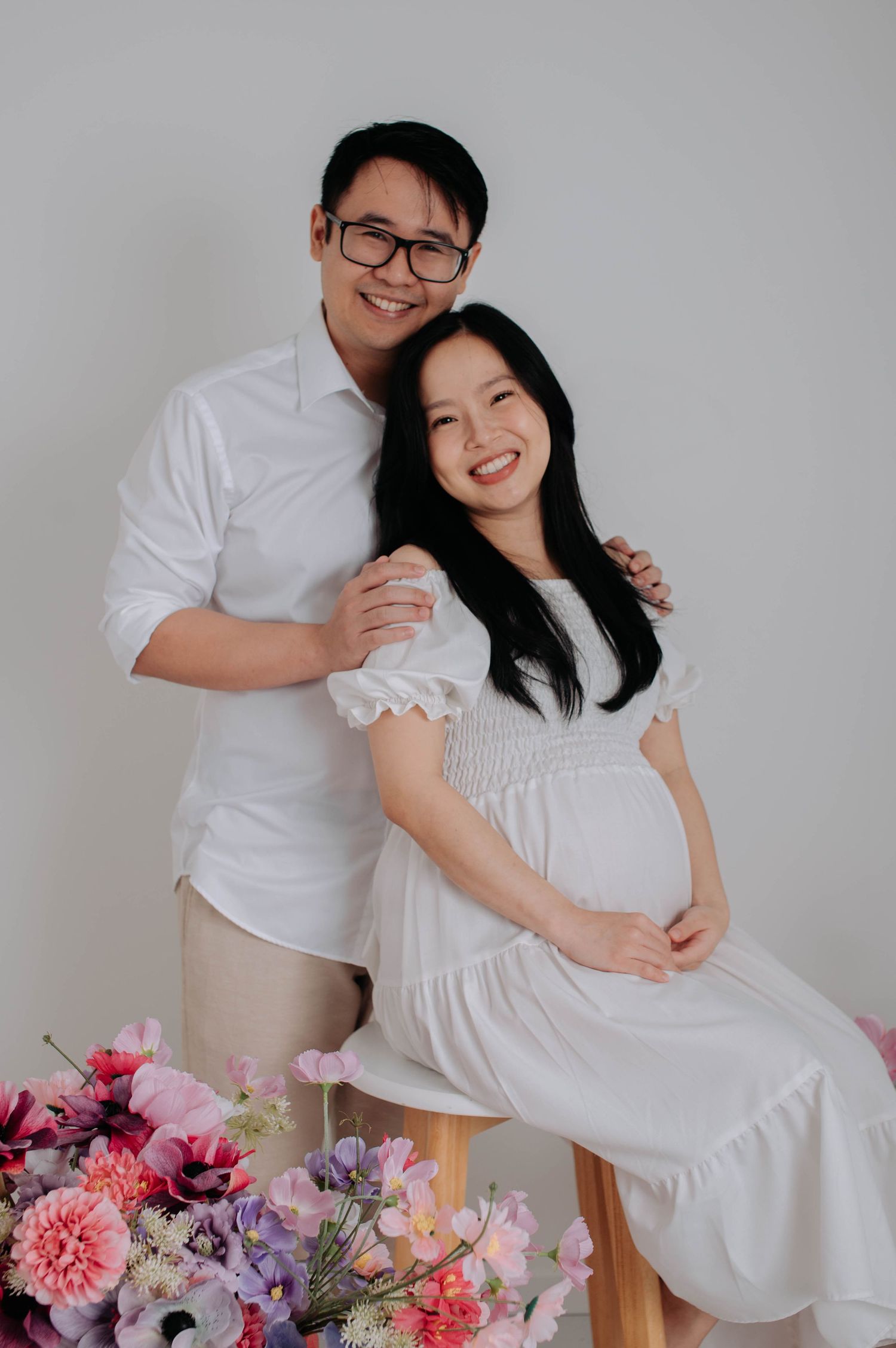 Maternity photoshoot with couple in white against floral decorations.