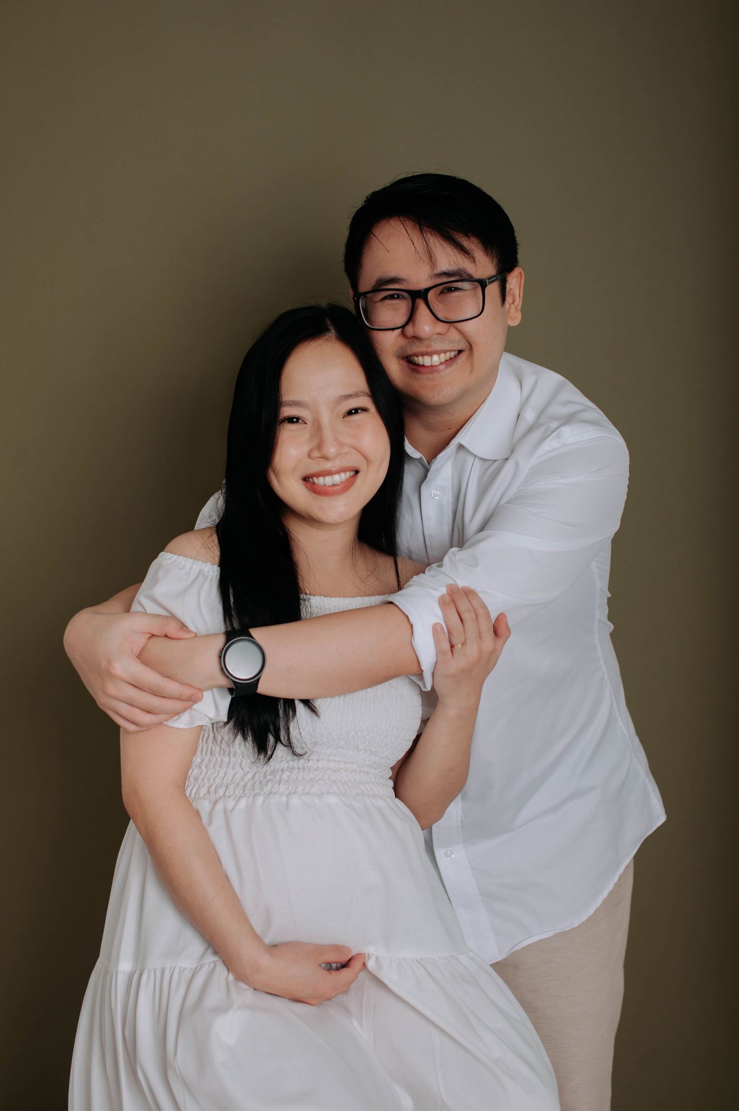 Couple embracing during maternity photo session against dark backdrop.