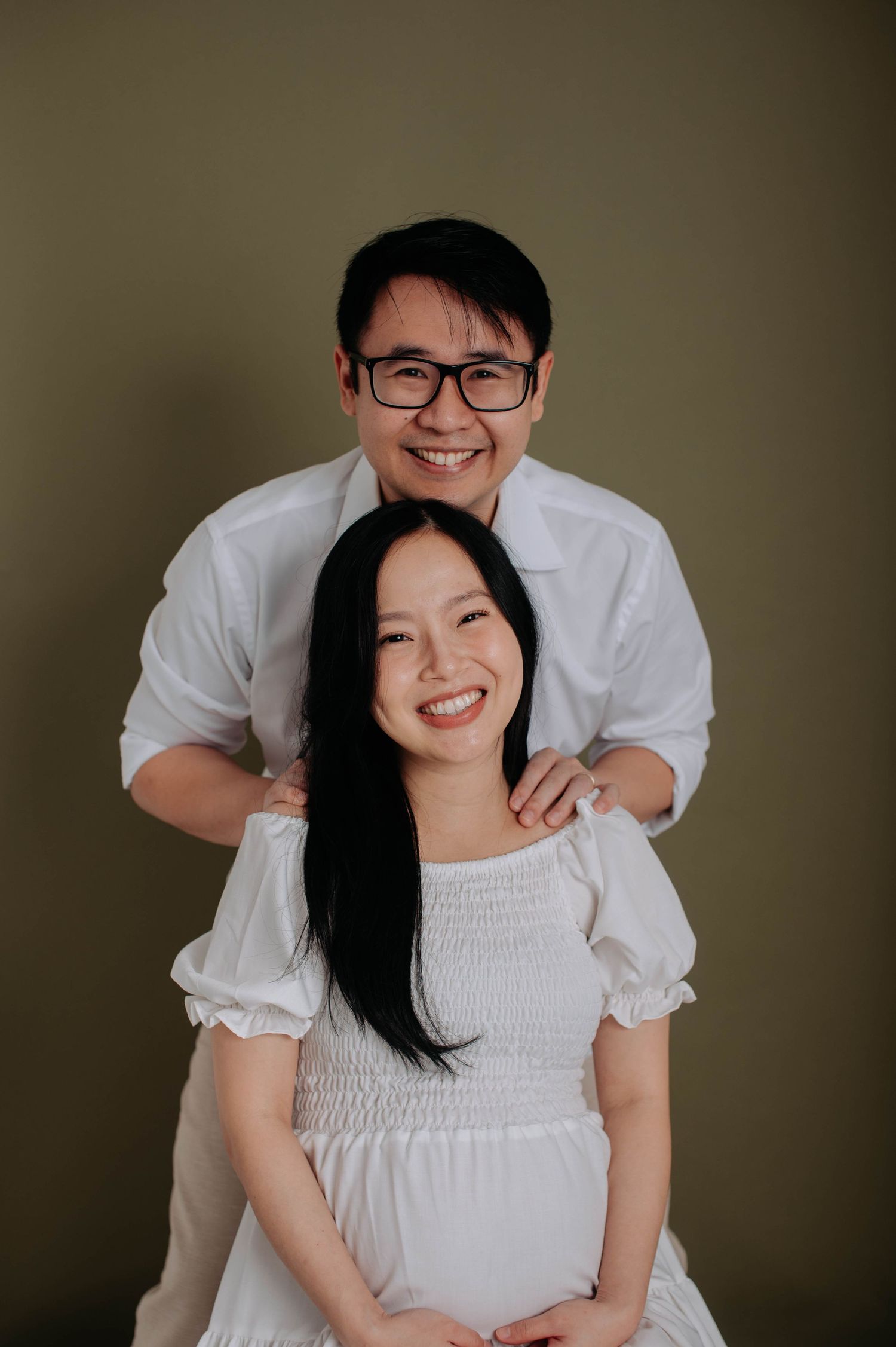 Couple embracing in studio maternity photoshoot against dark background.