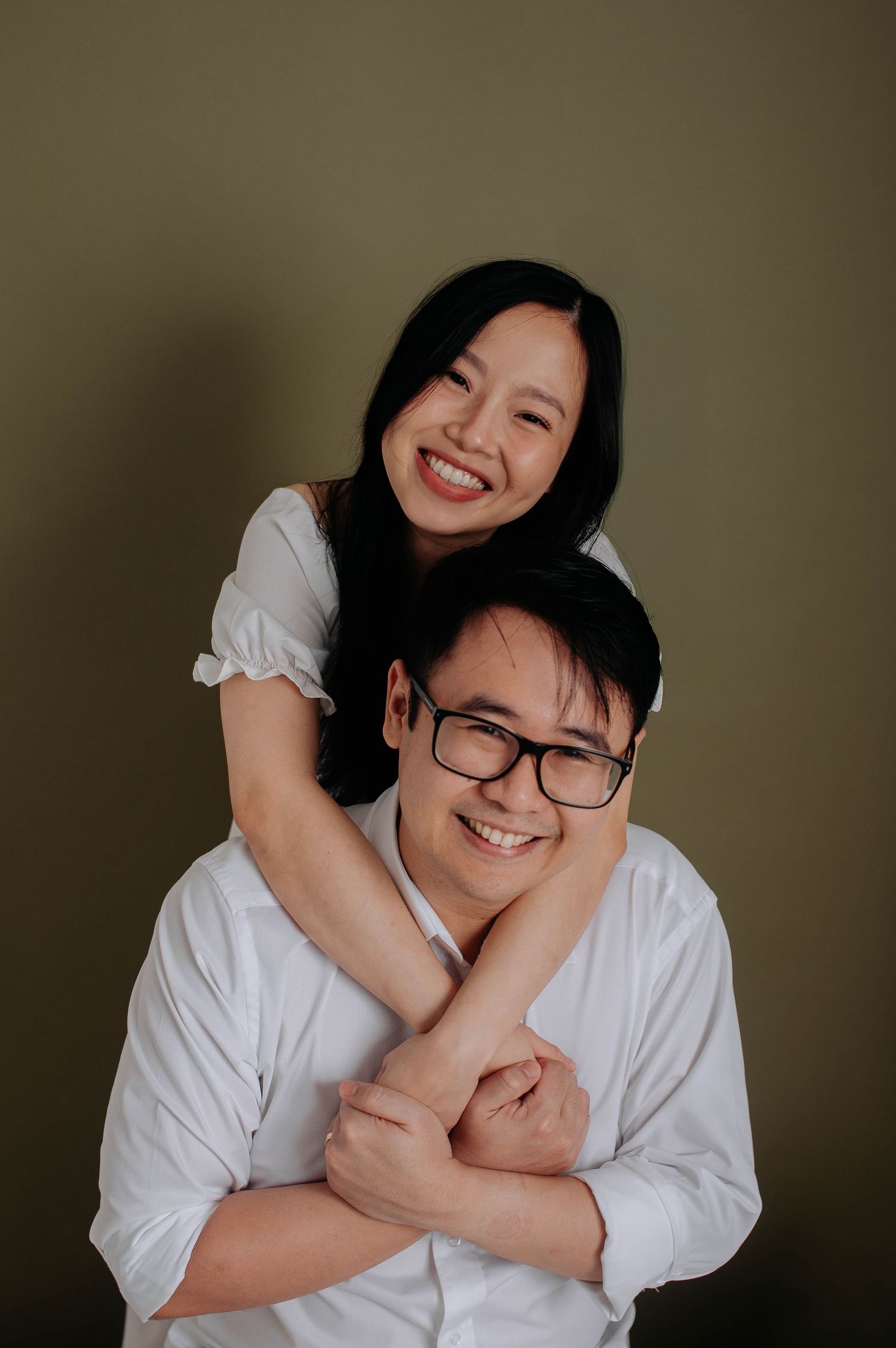 Intimate maternity portrait with couple sharing joyful laughter against brown backdrop.