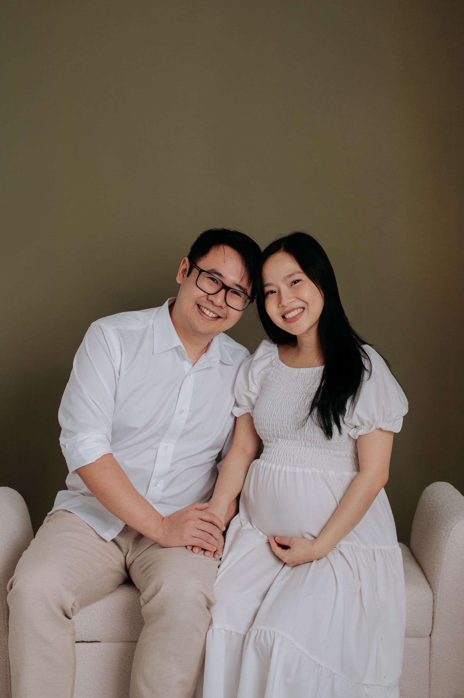Couple sitting on beige couch during pregnancy photoshoot.