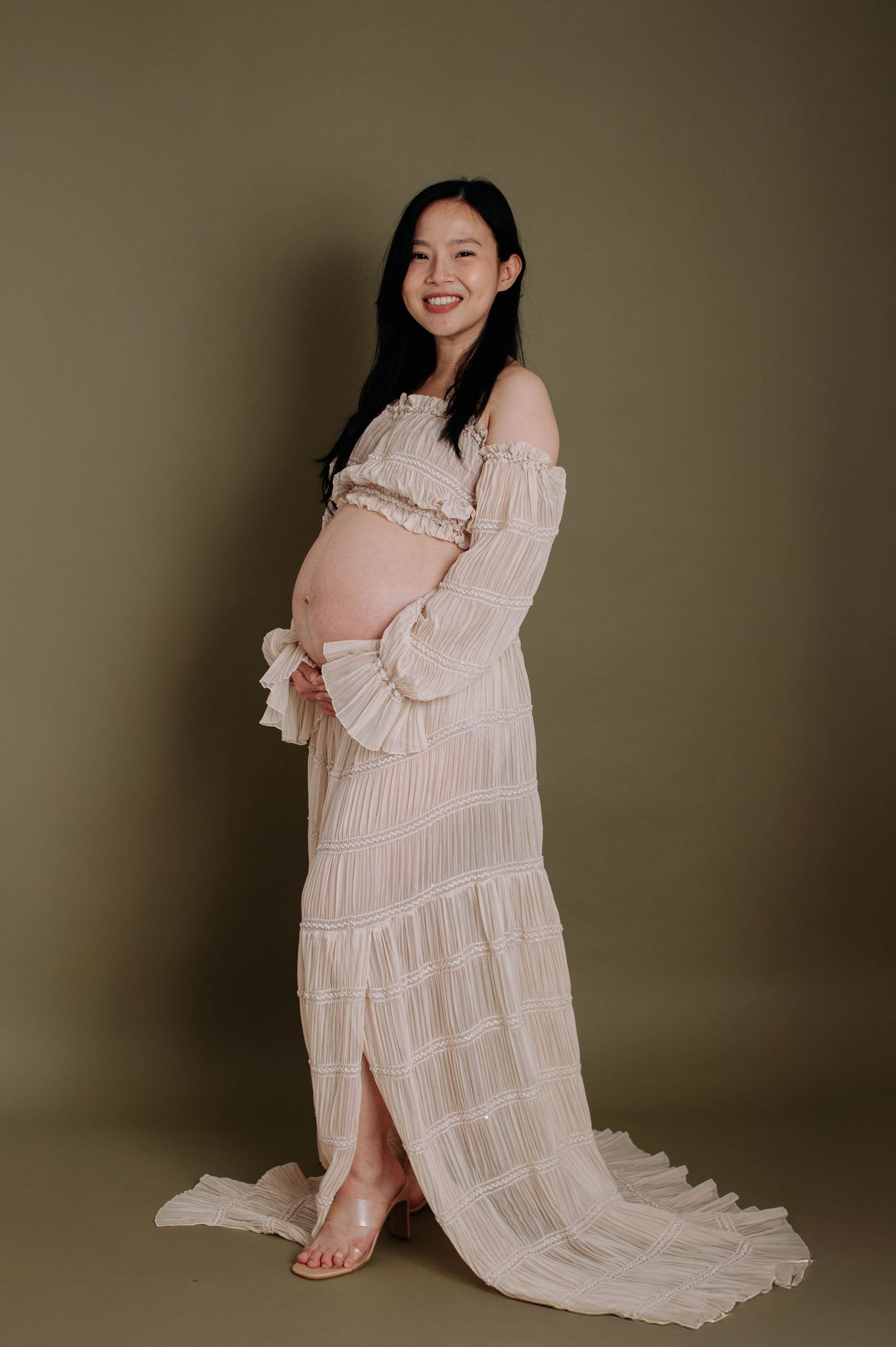 Side view of pregnant woman in flowing beige dress against dark background.
