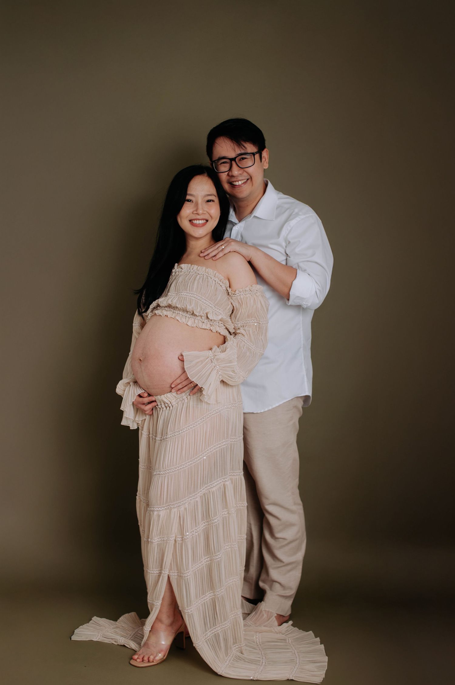 Maternity portrait with couple in neutral tones against dark background.