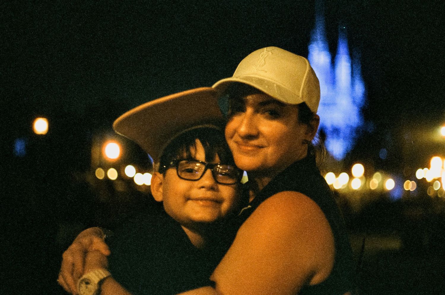 Two people embrace in a nighttime photo with bokeh lights and a blue glow in the background.