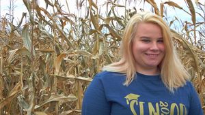 Person in blue sweatshirt smiling in front of dried corn stalks.