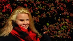 Person wearing red plaid scarf against dark foliage background.