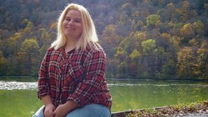Person in plaid shirt sitting by scenic mountain lake in autumn.