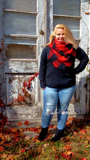 Person in black sweater and plaid scarf poses against weathered white door frame.