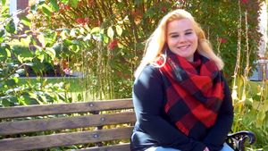 Person in navy sweater with red scarf sits on wooden bench outdoors.