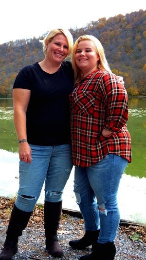 Two people in casual wear posing by a scenic lake with mountains in autumn.