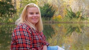Outdoor portrait session by lake with fall foliage and mountain backdrop.