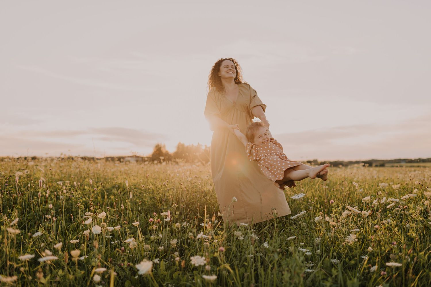 Two figures twirl together in a sunlit wildflower meadow at sunset.