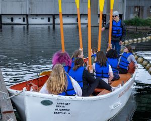 A group of people in life jackets paddling a boat with orange poles.