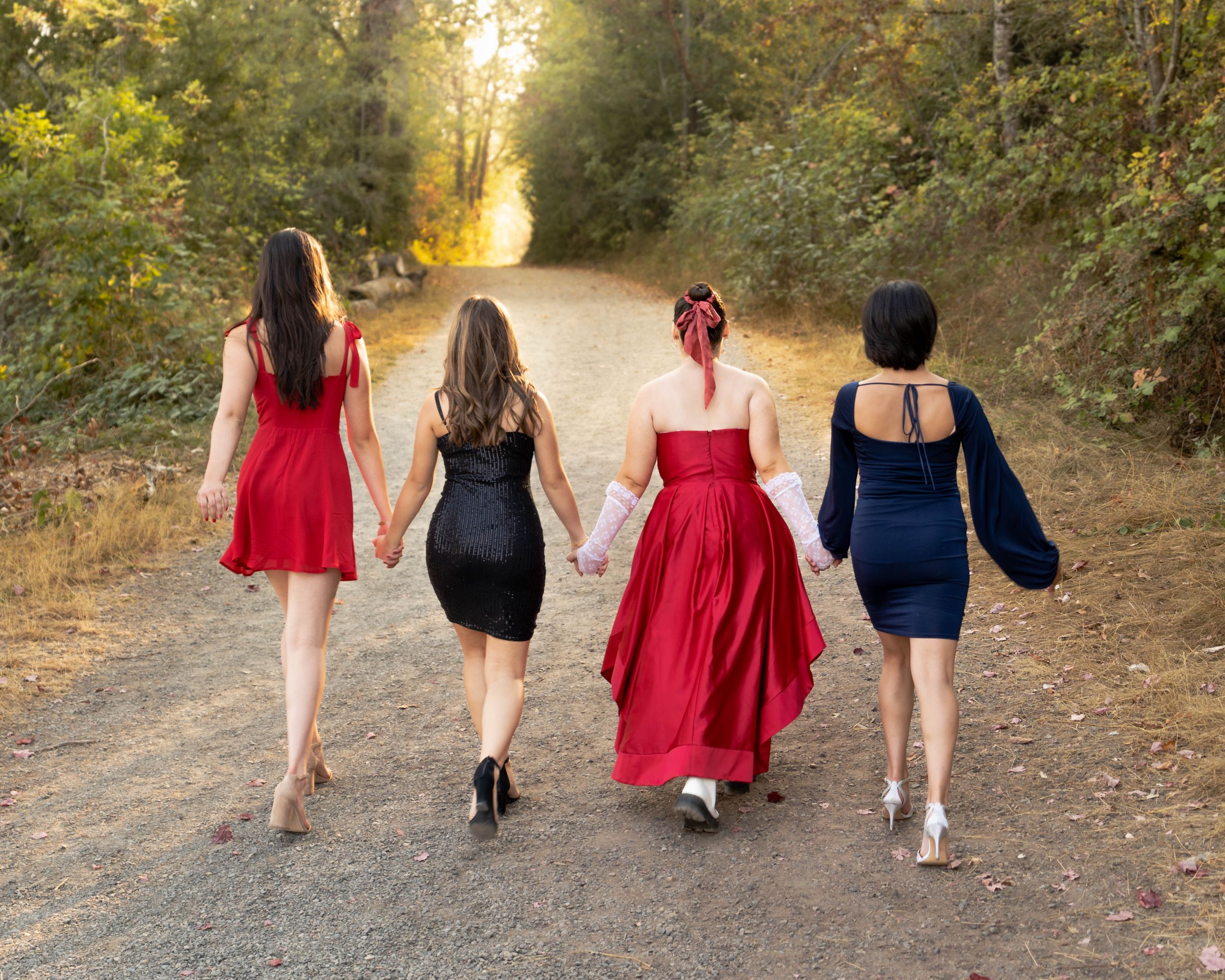 Friends in coordinating dresses walk down a sunlit forest path together.